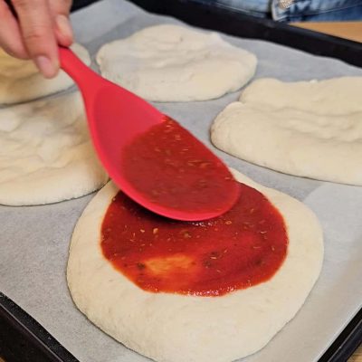 Salsa di pomodoro e origano stesa sulle pizzette senza glutine prima della cottura.