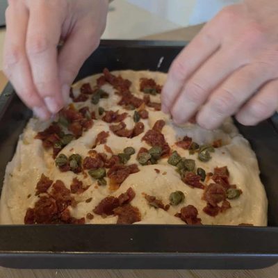metto capperi e pomodori sulla superficie della focaccia senza glutine mediterranea